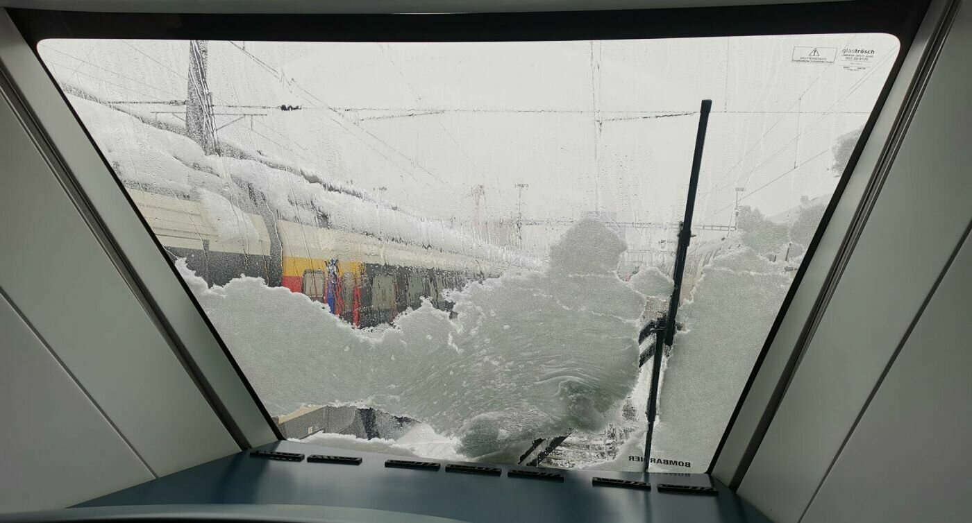 Blick aus einem mit Schnee bedeckten Zugfenster.