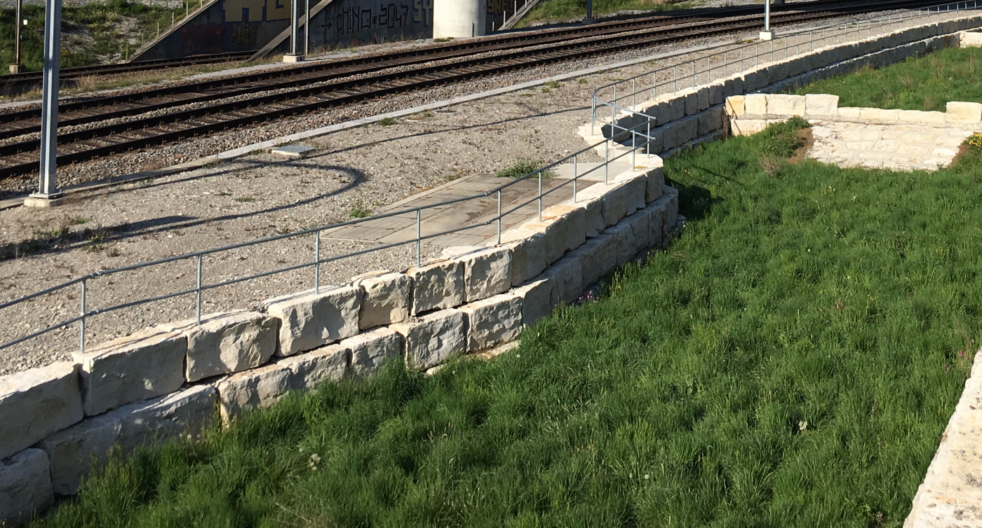 Pelouse naturelle à côté de la voie ferrée, séparée par un profond mur de pierre