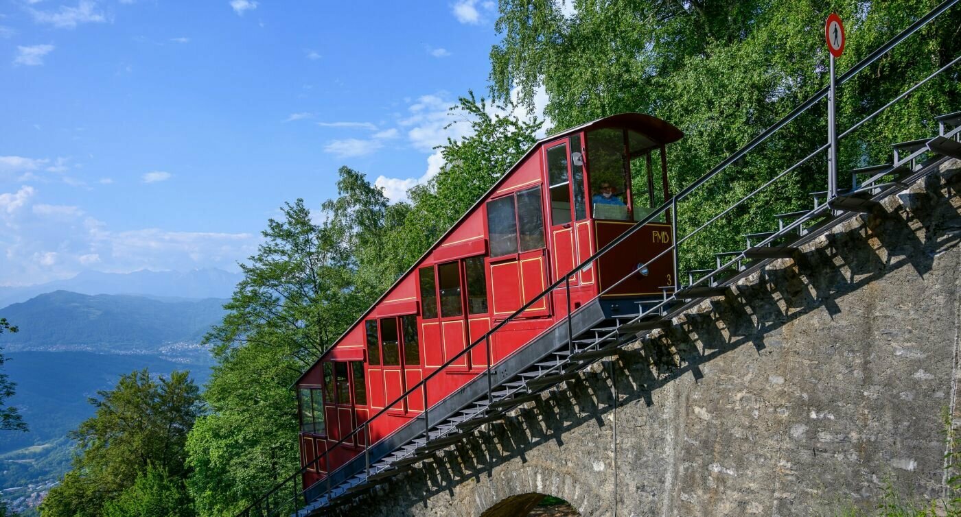 Eine rote historische Standseilbahn erklimmt die steile Bahnstrecke auf den Monte Brè.