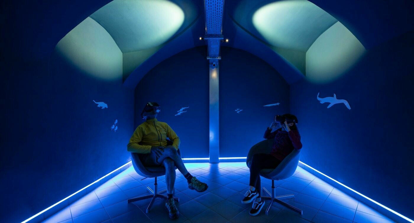 Salle éclairée en bleu avec deux personnes sur des chaises portant des lunettes VR