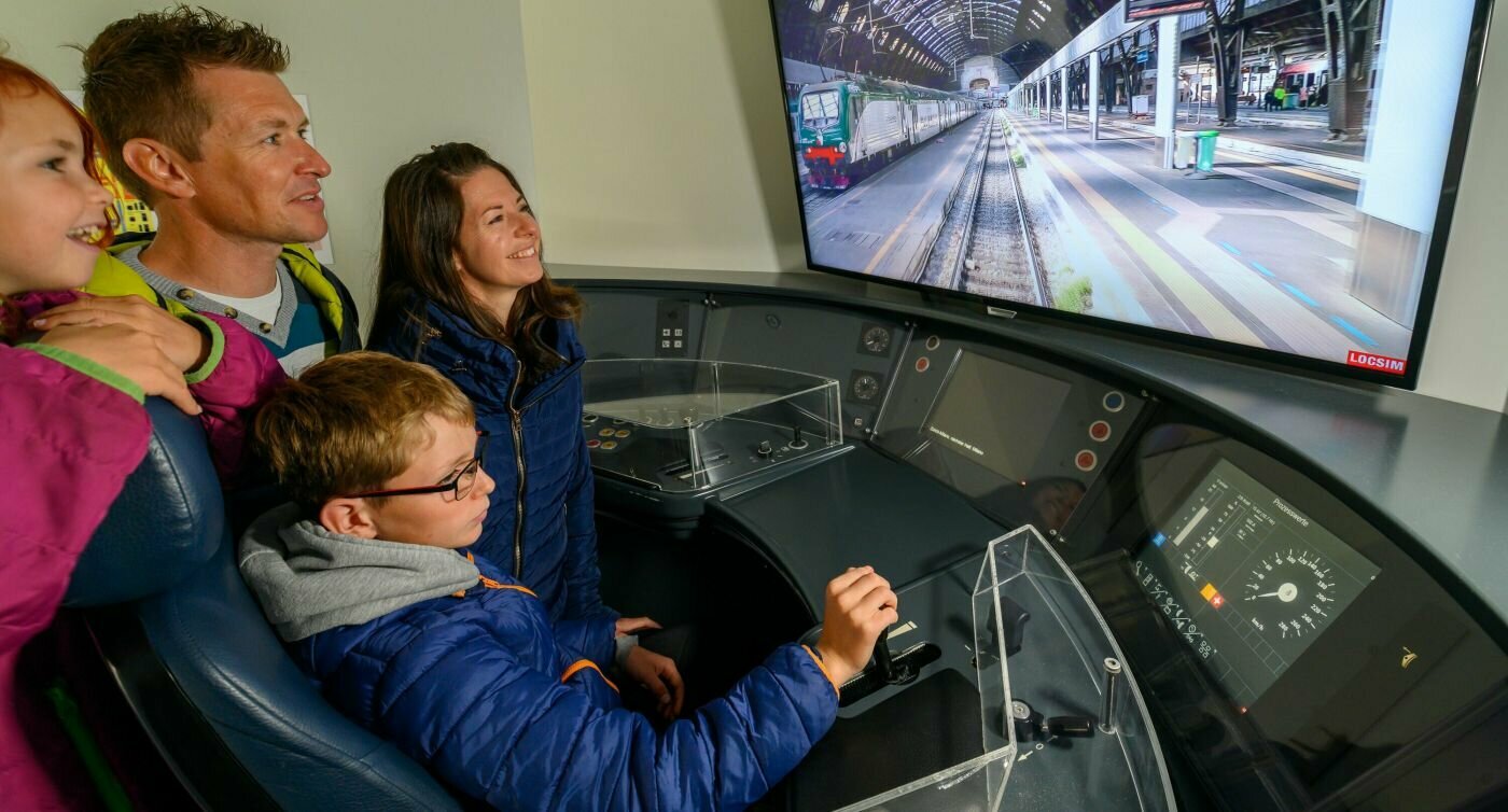 Une famille dans le simulateur de conduite de train au Musée des Transports de Lucerne. Le garçon manie le levier de commande, tandis que sa mère, son père et sa sœur regardent l’écran.