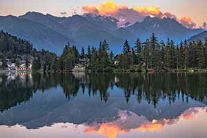 Sonnenuntergang über Champex-Lac, der Himmel und der Wald spiegeln sich im ruhigen Wasser.