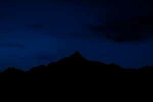 Une silhouette de montagne difficilement discernable sur un ciel nocturne.