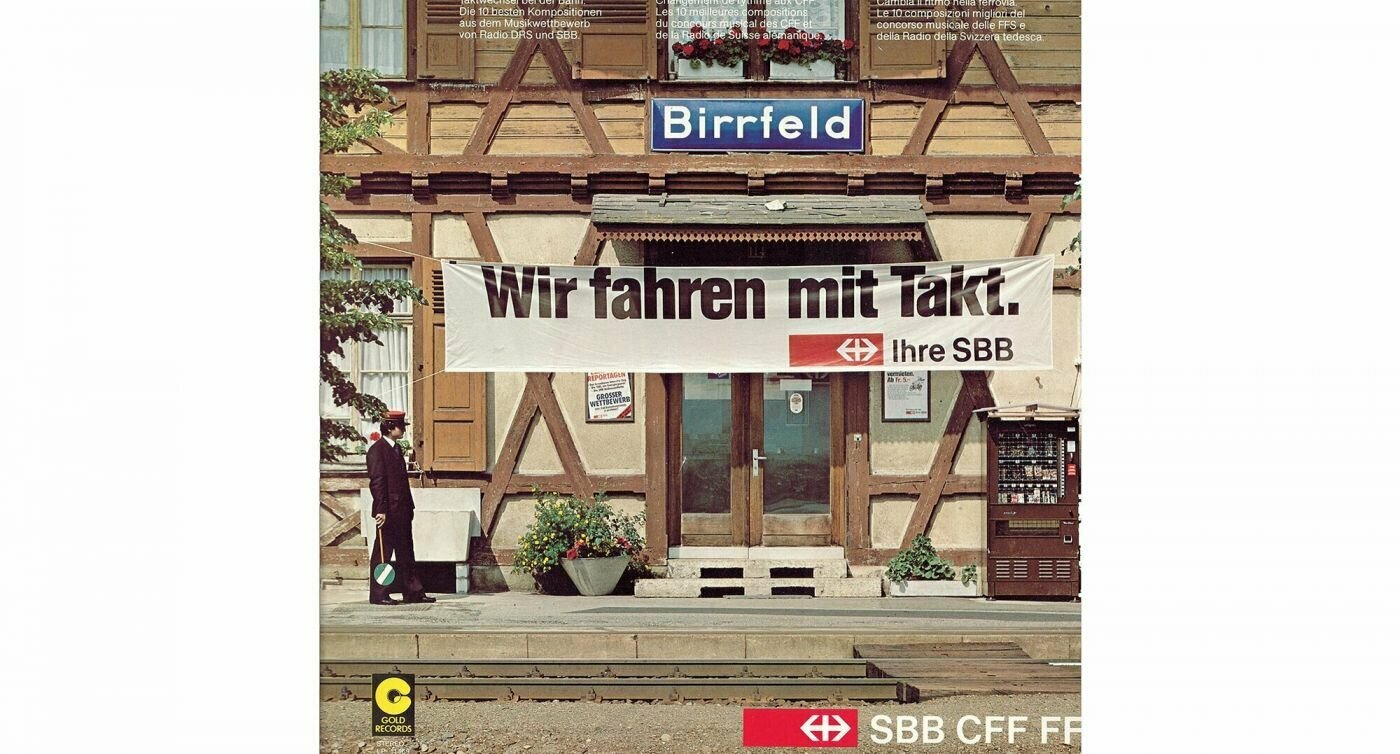 Affiche de l'entrée de la gare de Birrfeld avec une bannière "Nous roulons au rythme" en allemand