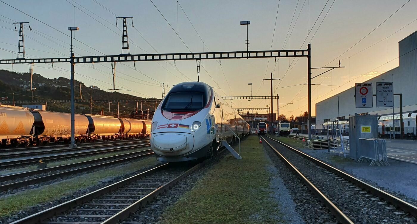 Zug steht bei Sonnenuntergang auf einem Gleis.