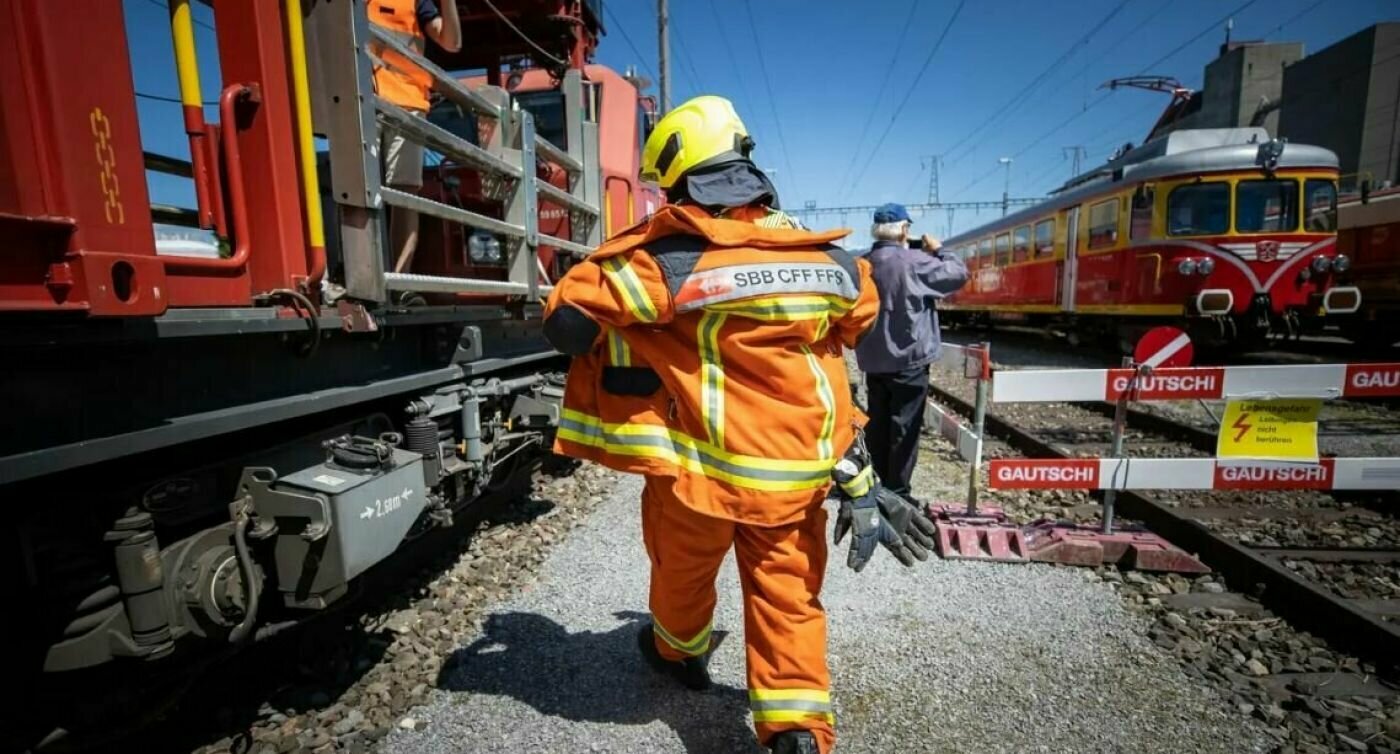 Un collaborateur CFF en tenue orange sur le gravier entre les trains.  