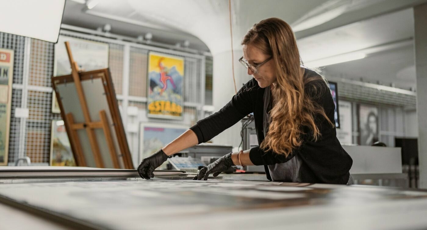 L’immagine mostra Andrea Kuratli mentre lavora al tavolo aspirante: fissa un manifesto con bande magnetiche