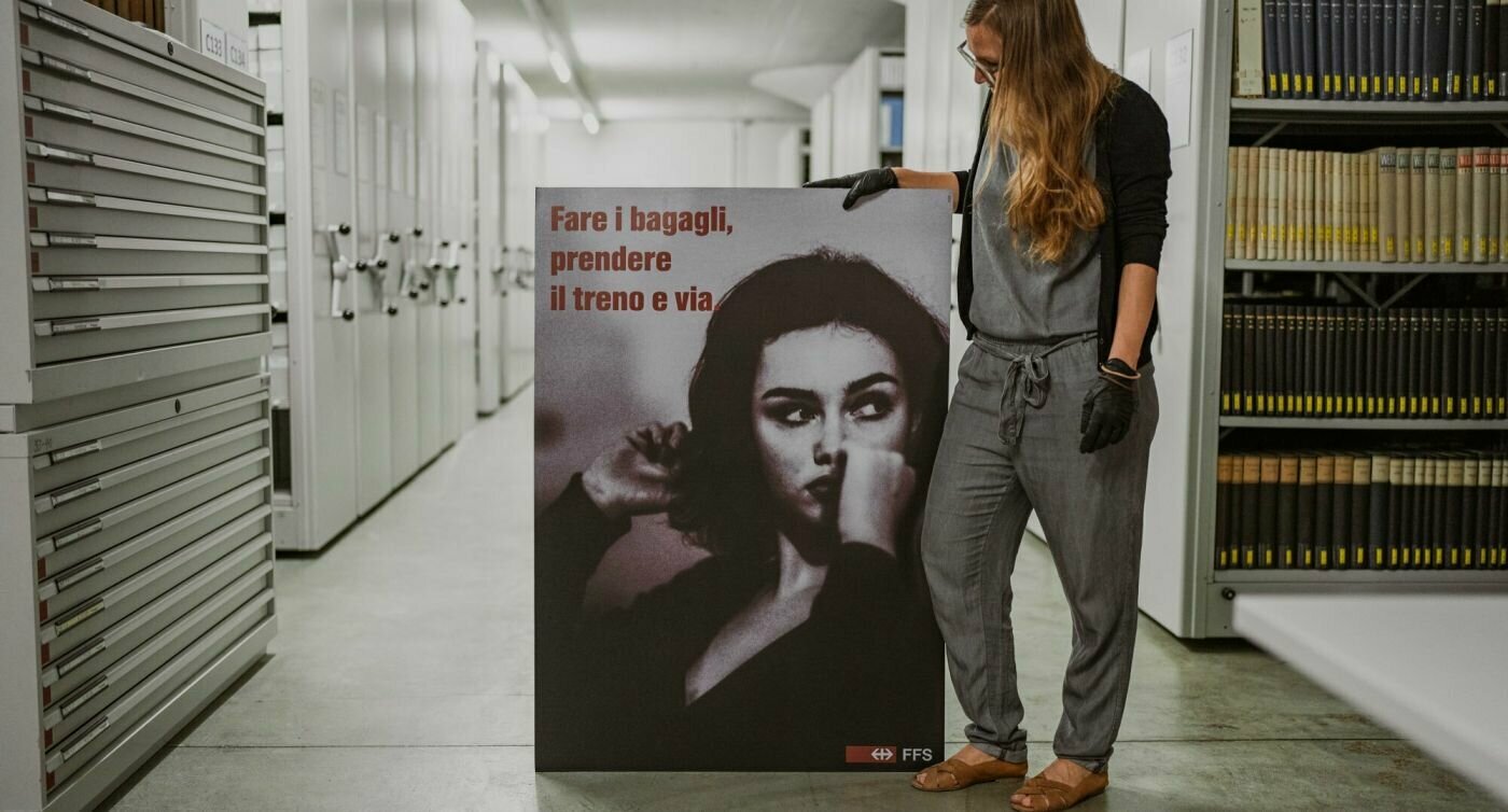 Andrea Kurati zeigt ein Plakat mit der Aufschrift "Packen Sie Ihre Koffer, nehmen Sie den Zug und fahren Sie los" auf Italienisch