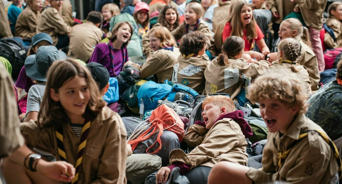 Un groupe de scout·e·s est assis sur le quai et chante.