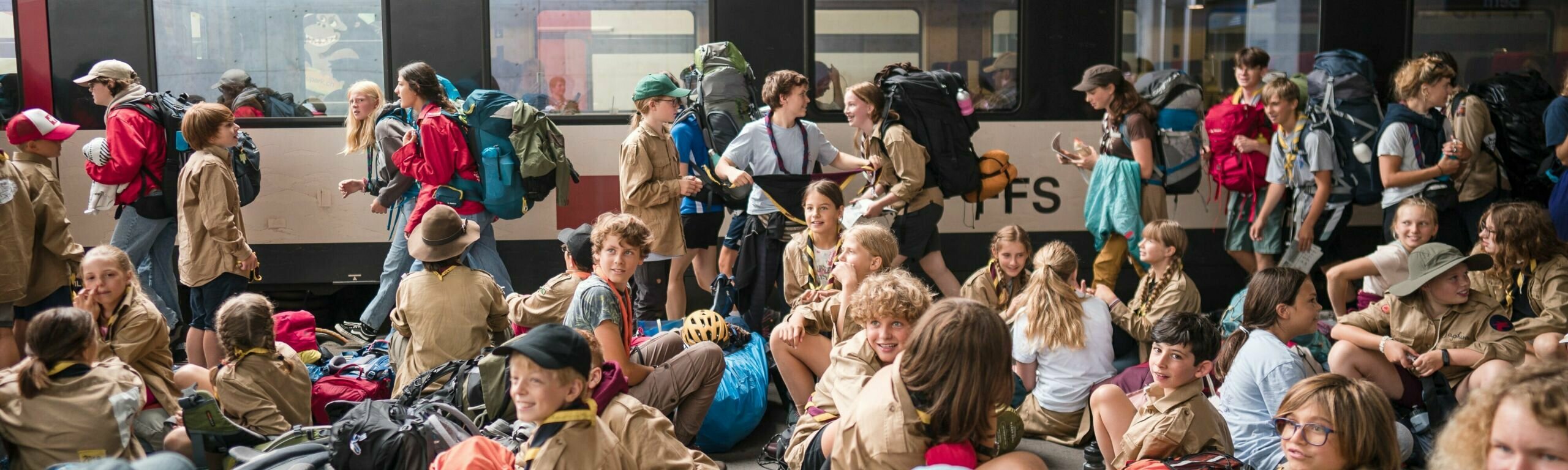 Un groupe de scout·e·s attends sur le quai avant de prendre le train