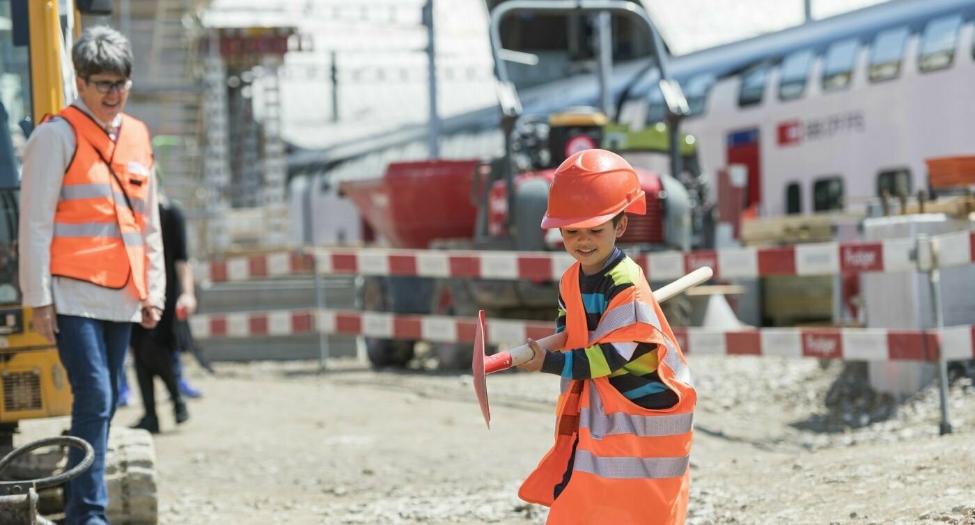 Ein Junge ist als Bauarbeiter verkleidet und spielt mit Werkzeug auf der Baustelle.