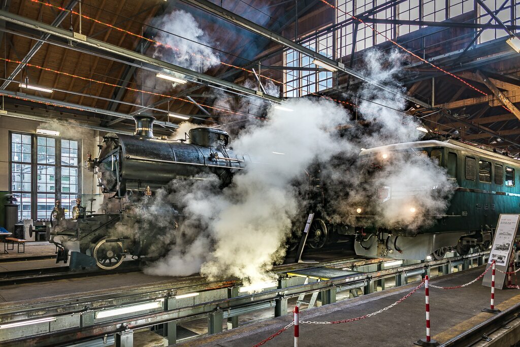 Rauchende Dampflokomotive und elektrische Lokomotive im Depot Erstfeld.
