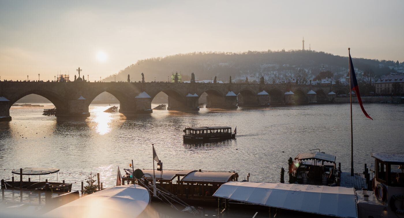 Un pont au-dessus de la Vltava. Un jour d'hiver, le soleil brille et un bateau traverse la rivière.