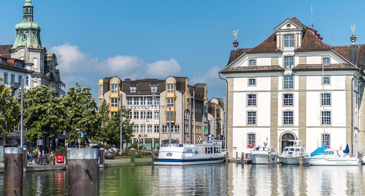 Vue depuis un ponton du lac de Constance sur le Kornhaus avec quelques bateaux amarrés devant le bâtiment.