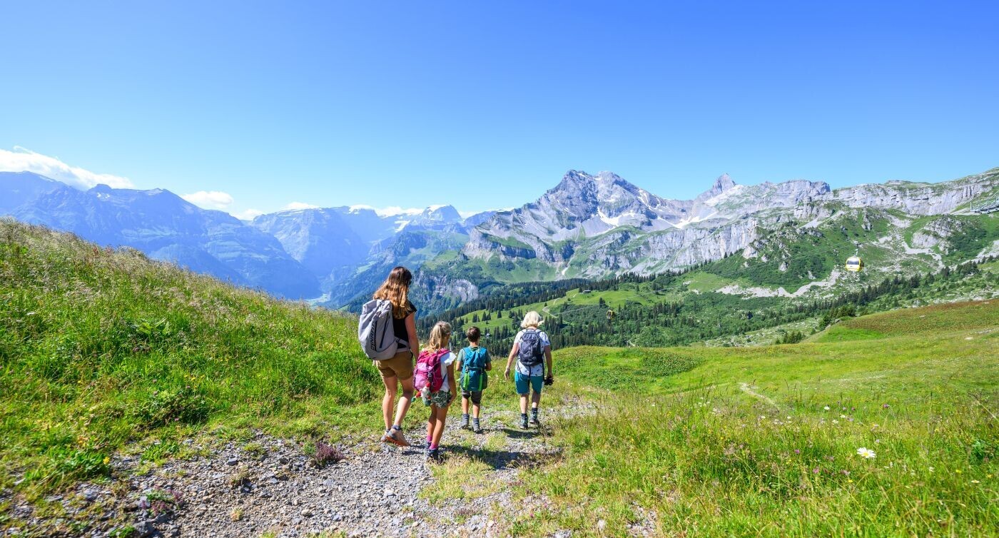 Eine kleine Gruppe Wanderer mit Kindern auf einem Bergpfad. Im Hintergrund die Glarner Alpen.