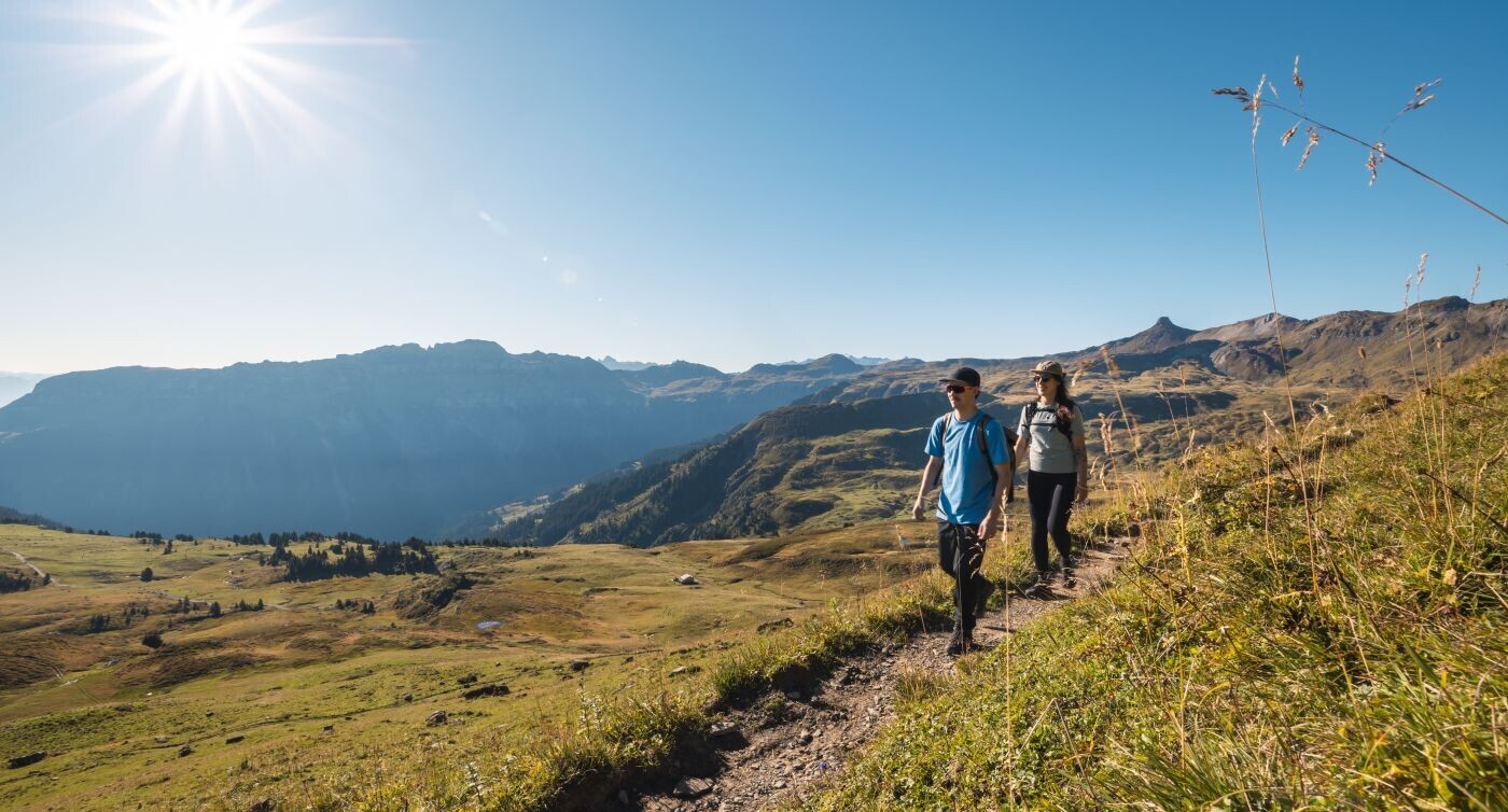Un homme et une femme marchent sur la crête d’une montagne sous le soleil. D’autres montagnes sont visibles en arrière-plan. 