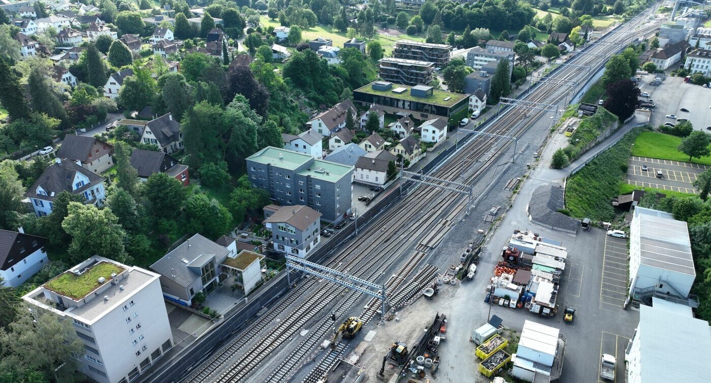 Luftaufnahme der Zufahrt zum Bahnhof Liestal von Basel aus. Die Gleise verzweigen sich zu den Bahnsteigen, umgeben von Gebäuden. Rechts ist das unangebundene Gleis 1 erkennbar.
